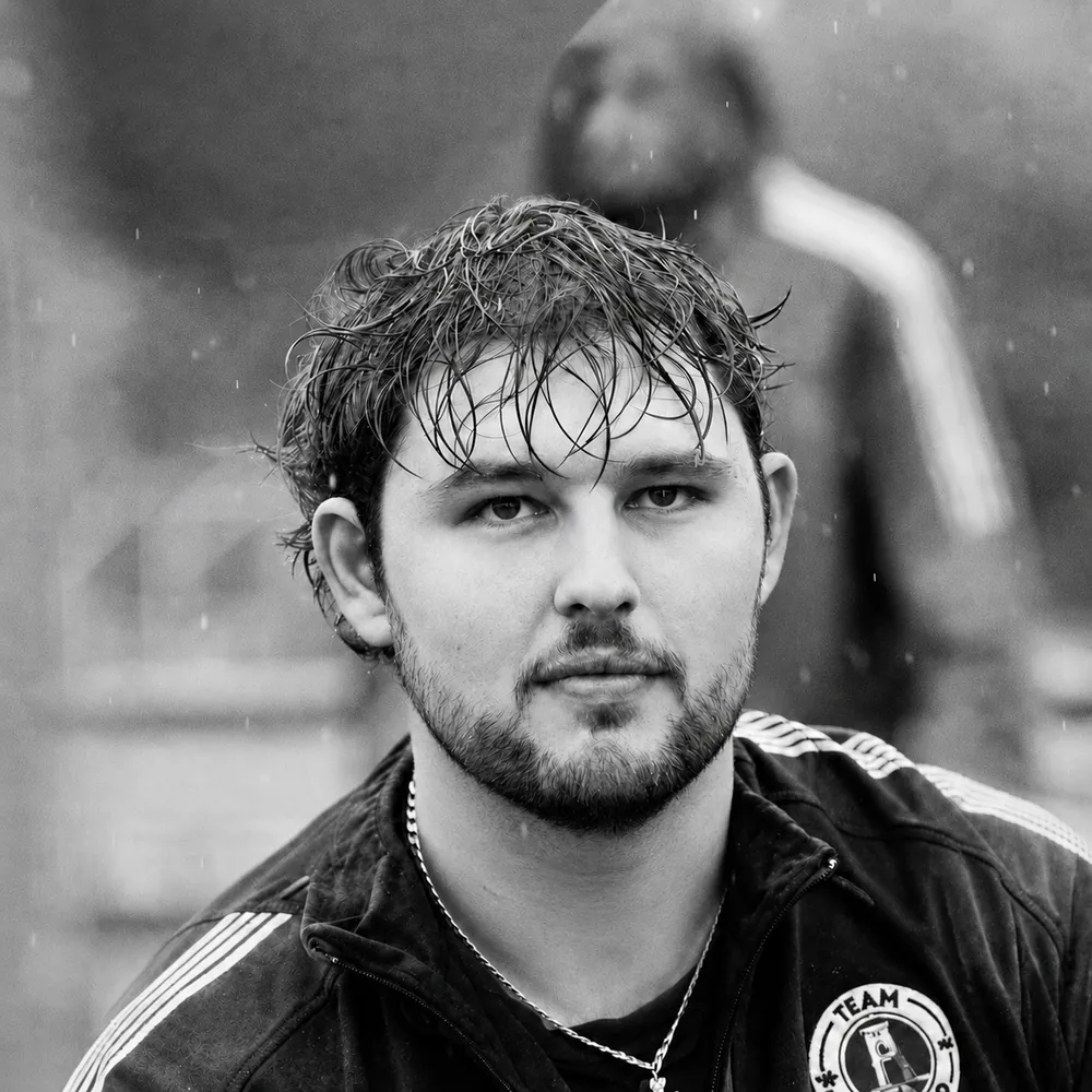 Brydon Duncan, black-and-white close-up portrait with rain-soaked hair, wearing a team track jacket